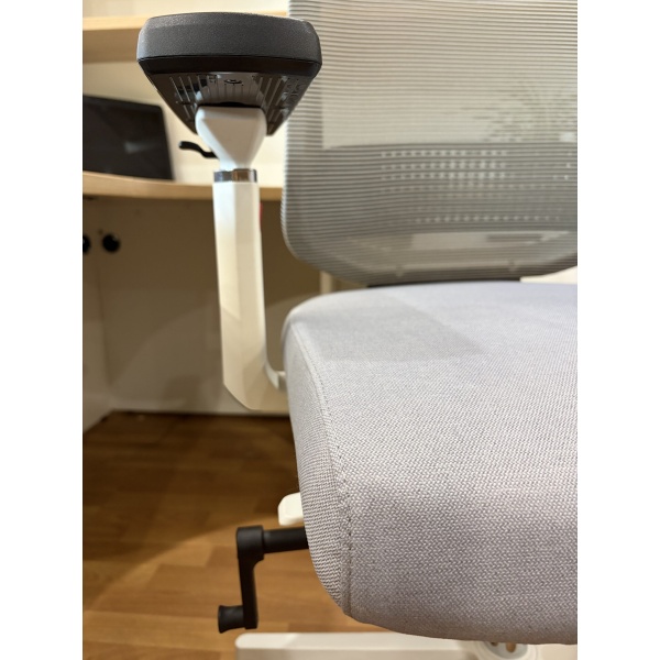 Harpo chair close-up side view of an ergonomic office chair featuring a grey mesh backrest, grey fabric seat, white frame, and adjustable armrest in a modern office workspace.